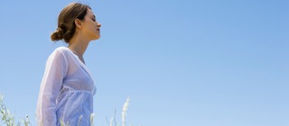 Eine Frau atmet tief auf einer Wiese vor bauem Himmel: Ohne Sauerstoff können wir nicht leben.