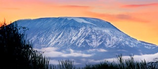 Schnee auf dem Kilimandscharo vor rosa-orangen Himmel: Auf der Erde gibt es verschiedene Klimazonen von den Polen bis zu den Tropen.