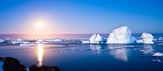 Kleine und große Eisberge schwimmen bei tiefstehender Sonne auf dem Meer. Weil Eis leichter ist als Wasser, schwimmen die Eisberge.