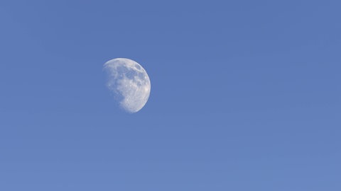 Der Mond am Tag über einer Tanne im Schnee: Warum sehen wir den Mond auch am hellichten Tag?