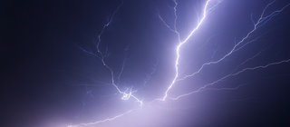 Ein großer Blitz zuckt am Nachthimmel über einem Feld auf. 