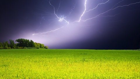 Ein großer Blitz zuckt am Nachthimmel über einem Feld auf.