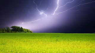 Ein großer Blitz zuckt am Nachthimmel über einem Feld auf. 