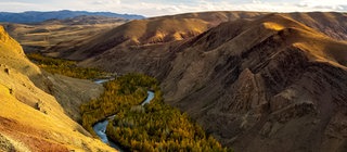 Ausblick auf ein Tal, durch das ein Fluss fließt. Das Wasser gräbt sich mit der Zeit immer tiefer in den Untergrund ein.