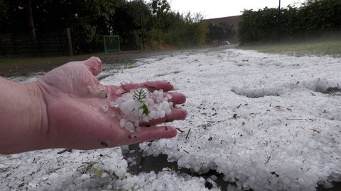 Hagelkörner bedecken eine Wiese. Damit Hagel entsteht braucht es niedrige Temperaturen und starke Winde.