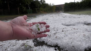 Hagelkörner bedecken eine Wiese. Damit Hagel entsteht braucht es niedrige Temperaturen und starke Winde.