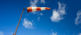Rot-weißer Windsack am blauen Himmel: Wie entsteht Wind? Was macht die Luft in der Erdatmosphäre?