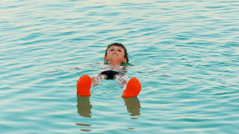 Ein Junge lässt sich auf der Wasseroberfläche treiben. Das Tote Meer ist so salzig, dass man auf dem Wasser liegen kann.