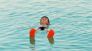 Ein Junge lässt sich auf der Wasseroberfläche treiben. Das Tote Meer ist so salzig, dass man auf dem Wasser liegen kann.
