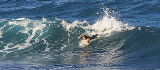 Ein Surfer paddelt durch eine große Welle. Wird der Wind zu stark und die Wellen zu hoch, kann es für Menschen gefährlich werden.