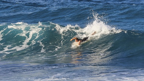 Ein Surfer paddelt durch eine große Welle. Wird der Wind zu stark und die Wellen zu hoch, kann es für Menschen gefährlich werden.
