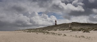 Der Strand von Sylt, im Hintergrund ein Leuchtturm. Würde der Mensch nichts unternehmen, dann würde die Insel im Laufe der Zeit vom Meer weggespült werden.