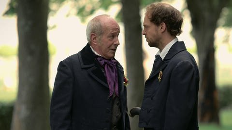 Zwei Männer in altertümlichen Anzügen unterhalten sich. (Foto: SWR – Screenshot aus der Sendung)