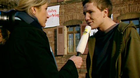 Eine blonde Frau mit Mikrophon in der Hand interviewt einen jungen Mann vor einem Backsteinhaus. Links im Bild ist eine Hand zu sehen, die eine Kamera hält. (Foto: SWR – Screenshot aus der Sendung)