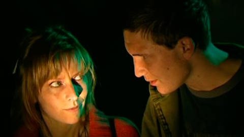Eine Frau in roter Jacke und ein jüngerer Mann stehen in einem dunklen Raum und sehen sich an. Nur die Gesichter sind angeleuchtet. (Foto: SWR – Screenshot aus der Sendung)