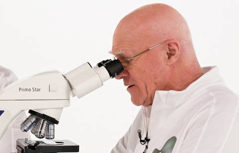 Ein Mann in einem weißen Kittel schaut in ein Mikroskop.