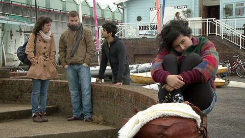 Eine junge Frau sitzt zusammengekauert auf einer Mauer, dahinter stehen drei junge Leute. (Foto: WDR/ footstep producction)