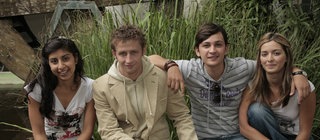 Vier junge Leute, zwei Mädchen und zwei Jungen, sitzen nebeneinander.