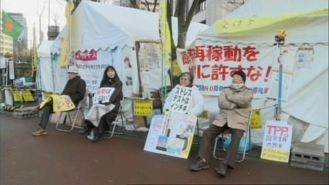 Japanische Demonstranten sitzen mit Plakaten vor Zelten.