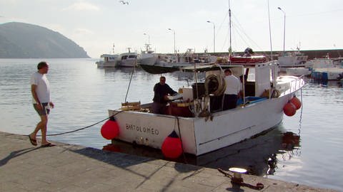 Drei Fischer mit einem kleinen Boot an einer Anlegestelle.