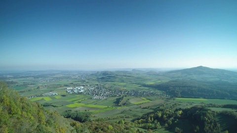 Blick von einem Hügel aus über eine weite, grüne Landschaft.
