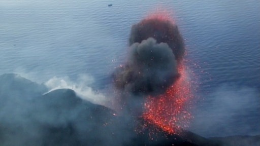 Rote Glut und graue Rauchwolken an einem Berg.