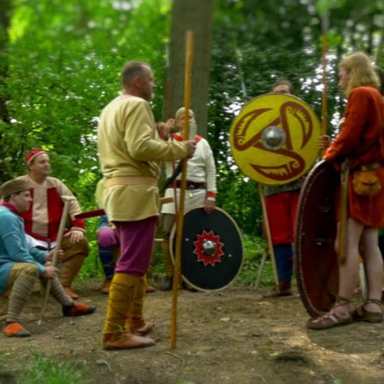 Spielszene: Farbenfreudig gekleidete Männer und Frauen debattieren im Wald. (Foto: SWR – Screenshot aus der Sendung)