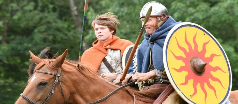 Ein keltisch gekleideter Mann und Junge reiten mit Schilden und Speren bewaffnet.