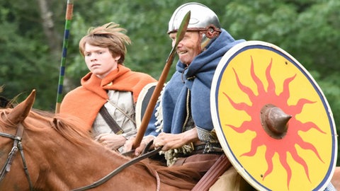 Ein keltisch gekleideter Mann und Junge reiten mit Schilden und Speren bewaffnet.