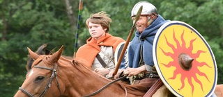 Ein keltisch gekleideter Mann und Junge reiten mit Schilden und Speren bewaffnet.