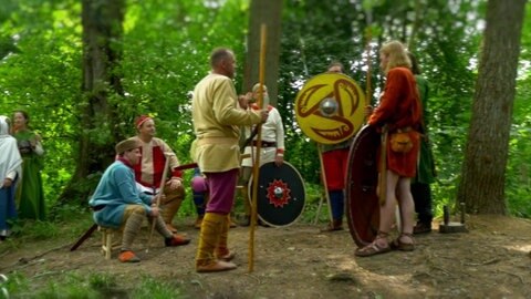 Spielszene: Farbenfreudig gekleidete Männer und Frauen debattieren im Wald.