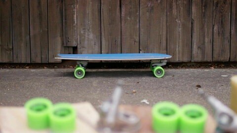 Surfskate vor Holzwand, im Vordergrund Bauteile.