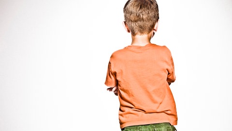 Blick auf den Rücken eines Jungen, der die Arme vor der Brust verschränkt hat