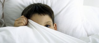 Ein Kind versteckt sich unter einer Bettdecke