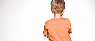 Blick auf den Rücken eines Jungen, der die Arme vor der Brust verschränkt hat