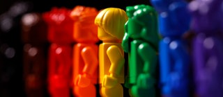 Plastikfiguren in den verschiedenen Farben des Regenbogens stehen nebeneinander als Symbol für Diversität
