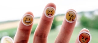 Auf die Finger einer Hand sind verschiedene Emojis aufgeklebt.