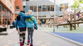Zwei Freundinnen gehen Arm in Arm über einen Schulhof