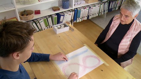 Junge und Lehrerin sitzen sich an einem Tisch gegenüber (Foto: SWR - Screenshot aus der Sendung)