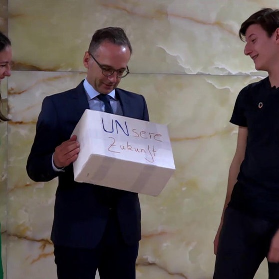 Josephine und Niklas übergeben Karton mit Aufschrift UNsere Zukunft an Außeminister Maas.