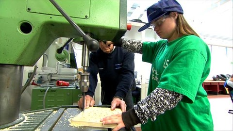 Sophie steht mit einem Mann an einer Stanzmaschine