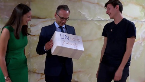 Josephine und Niklas übergeben Karton mit Aufschrift UNsere Zukunft an Außeminister Maas.