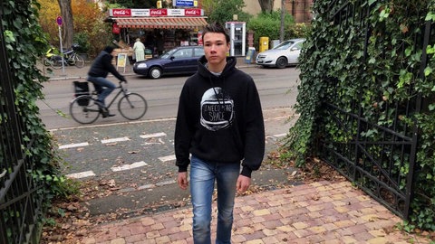 Zu sehen ist ein Junge in schwarzem Hoodie, der über die Straße geht.