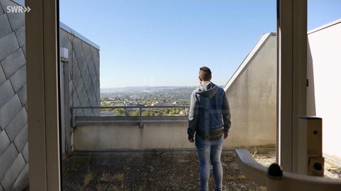 Mann steht auf einem Hochhausdach und blickt über die Brüstung