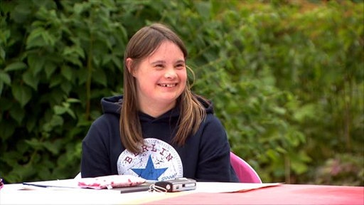 Sophie sitzt am Tisch und lacht.