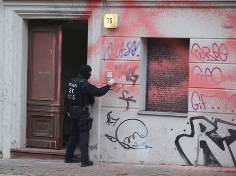 Polizisten tragen Karton an Hauswand entlang.