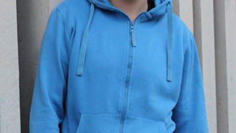 Julius, im blauen Kapuzenpulli, lächelt in die Kamera.