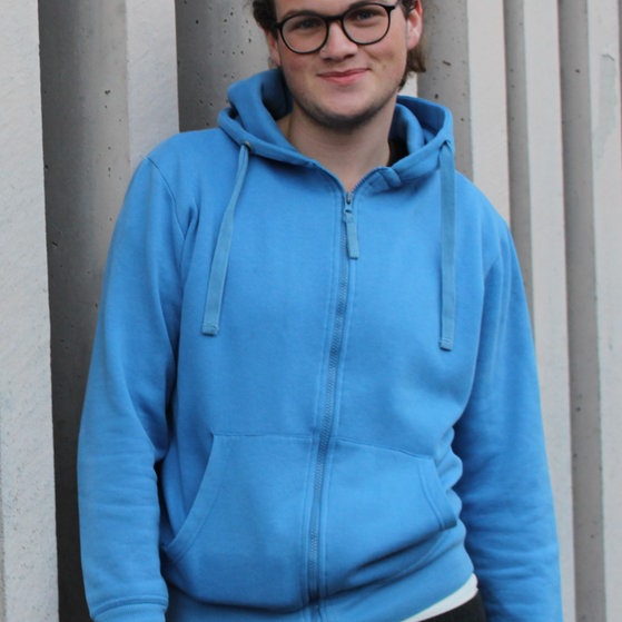 Julius, im blauen Kapuzenpulli, lächelt in die Kamera.