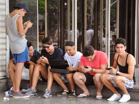 Mehrere junge Menschen sitzen auf einer Stufe und benutzen Handys oder einen Laptop (Foto: Imago)