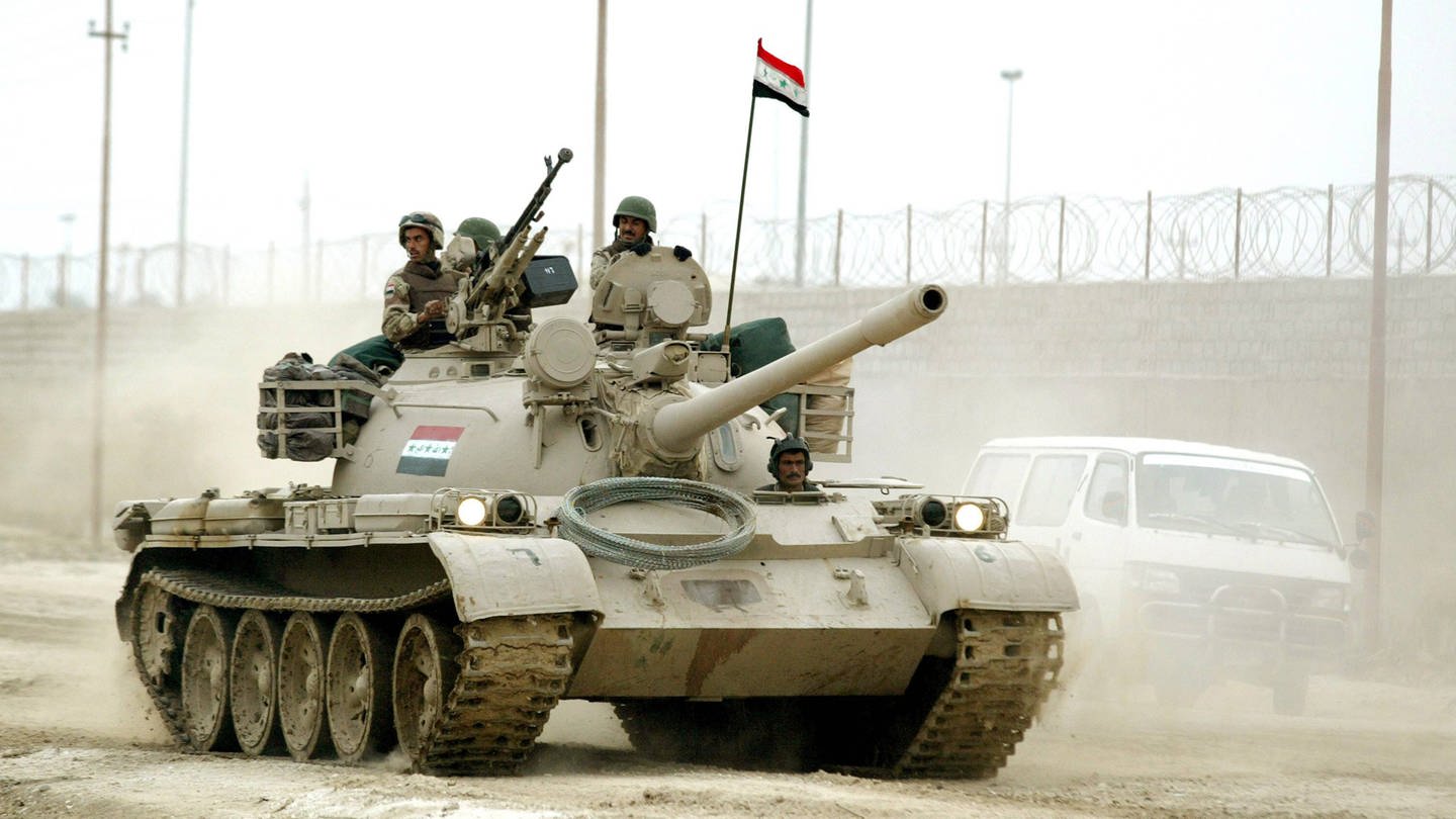Ein Panzer fährt durch eine staubige Straße in Bagdad, zwei Soldaten schauen hinaus. Internationale Krisen. (Foto: IMAGO / UPI Photo)